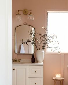 a bathroom with pink walls and white cabinetry has a large mirror on the wall