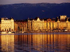 a large building sitting on top of a lake next to a tall mountain covered in clouds