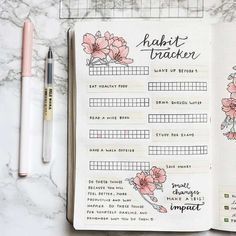 an open planner with pink flowers on it next to a pen and some other items