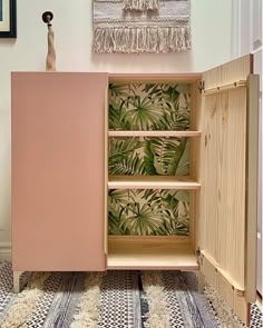 a pink cabinet with tropical wallpaper and rugs on the floor next to it