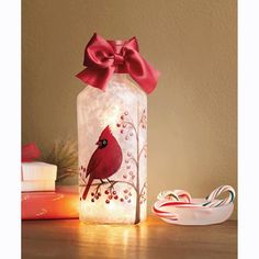 a lighted glass jar with a cardinal on it and some candy canes next to it