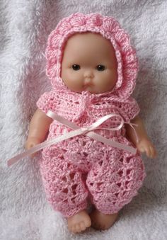 a baby doll wearing a pink crocheted outfit and bonnet on a white blanket