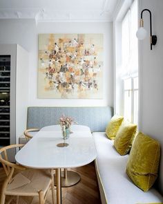 a white table with yellow pillows and a painting on the wall above it in a dining room