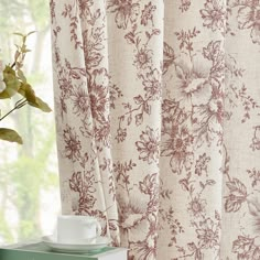 a vase with flowers on top of a table next to a book and window curtain