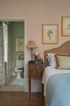 a bedroom with pink walls and pictures on the wall above the bed, along with a white toilet