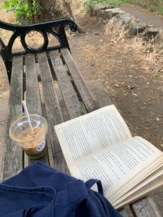 an open book sitting on top of a wooden bench next to a cup of coffee