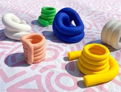 several different colored plastic objects sitting on a pink and white tablecloth with an intricate design