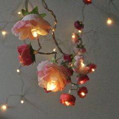 some lights are hanging from a branch with flowers on it and one light is turned on