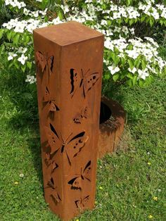 a rusted metal sculpture sitting on top of a lush green field next to white flowers