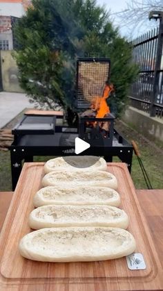 some bread sitting on top of a wooden cutting board next to a fire pit and grill