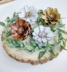 three flowers are sitting on top of a piece of wood with leaves and branches around it