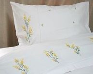 a bed with white sheets and yellow flowers on the pillowcase, along with two pillows