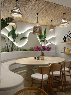 a round table surrounded by white chairs in a room with plants and potted plants