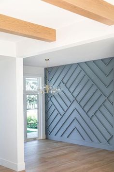 an empty room with wood flooring and blue wall paneling in the center, next to a chandelier