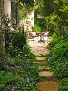 an image of a garden scene with flowers and plants in the foreground, along with a stone path leading to a patio