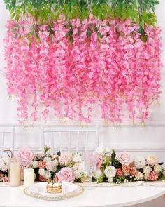 pink flowers are hanging from the ceiling above a table with cake and candles on it