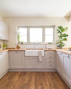 a kitchen with wooden floors and white cabinets, an oven, dishwasher, sink and potted plant