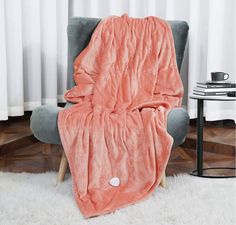 an orange blanket sitting on top of a chair next to a white rug and table