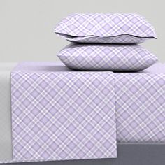 three pillows stacked on top of each other next to a bed with purple and white plaid sheets