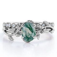 a ring with an oval green stone surrounded by leaves and diamonds on the sides, set in white gold