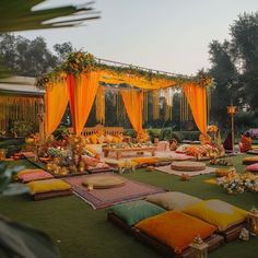 an outdoor wedding setup with yellow draping and orange pillows on the ground, surrounded by greenery