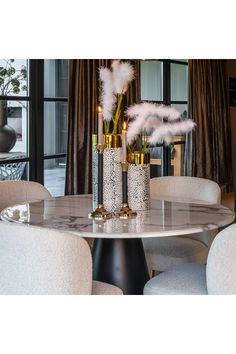 three tall vases with feathers on top of a marble table