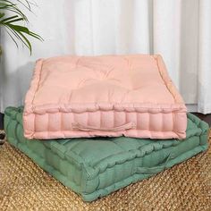 two pillows stacked on top of each other in front of a potted palm tree