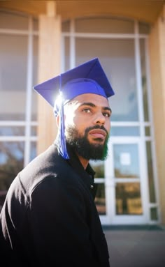 a man wearing a graduation cap and gown standing in front of a building with large windows