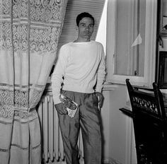 a man standing in front of a window next to a piano and curtain with the curtains open