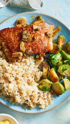 a blue plate topped with meat and rice next to brussel sprouts