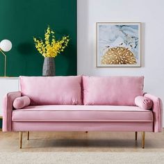 a pink couch sitting in front of a green wall next to a vase with yellow flowers