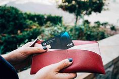 a woman holding a red wallet with two credit cards in it and her hand on the other side