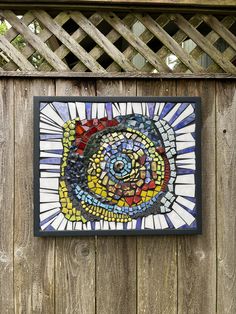 a stained glass piece hanging on the side of a wooden fence