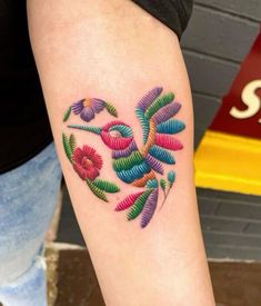 a colorful tattoo on the arm of a woman's left arm with flowers and leaves