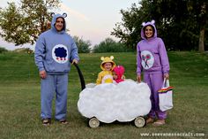 two adults and one child in costumes standing next to a wagon with sheep on it