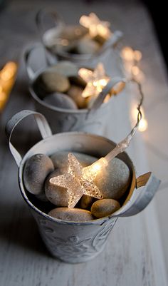 three metal buckets filled with rocks and lite up candles on top of a table