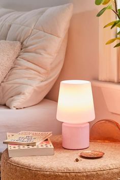 a pink lamp sitting on top of a wooden table next to a white bed and pillows