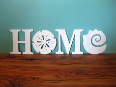 a wooden sign that says home with sand dollar and starfish on it in front of a blue wall