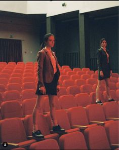 two women standing in an auditorium with red chairs