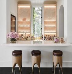 two stools sitting in front of a bar with bottles on the counter and flowers