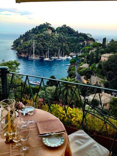 an outdoor dining area overlooking the ocean and boats in the water, with a table set for two