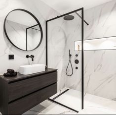 a bathroom with marble walls and flooring is shown in black and white, along with a round mirror on the wall