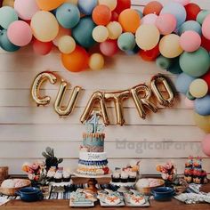 a young boy sitting in front of a cake surrounded by balloons and cupcakes