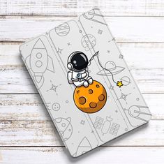 an ipad case with an astronaut on the moon and rockets in space, sitting on top of it