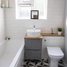 a white toilet sitting next to a bath tub under a window near a sink with a wooden counter top