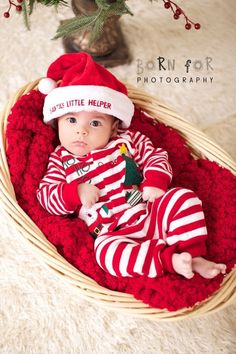 a baby wearing a santa hat in a basket with red and white striped pajamas on