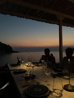 two people sitting at a table with wine glasses in front of them and an ocean view