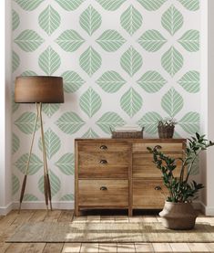 a room with a dresser, lamp and green leaves wallpaper on the wall behind it