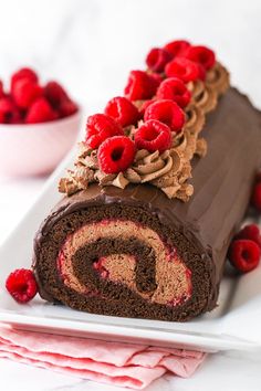 a chocolate roll with raspberries on top is sitting on a plate next to some strawberries