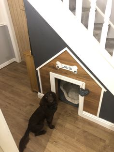 a dog is sitting in his house under the stairs